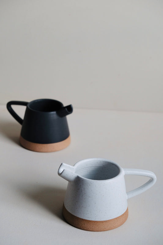 Two ceramic pitchers, one black and one white with brown base, on a light gray surface.