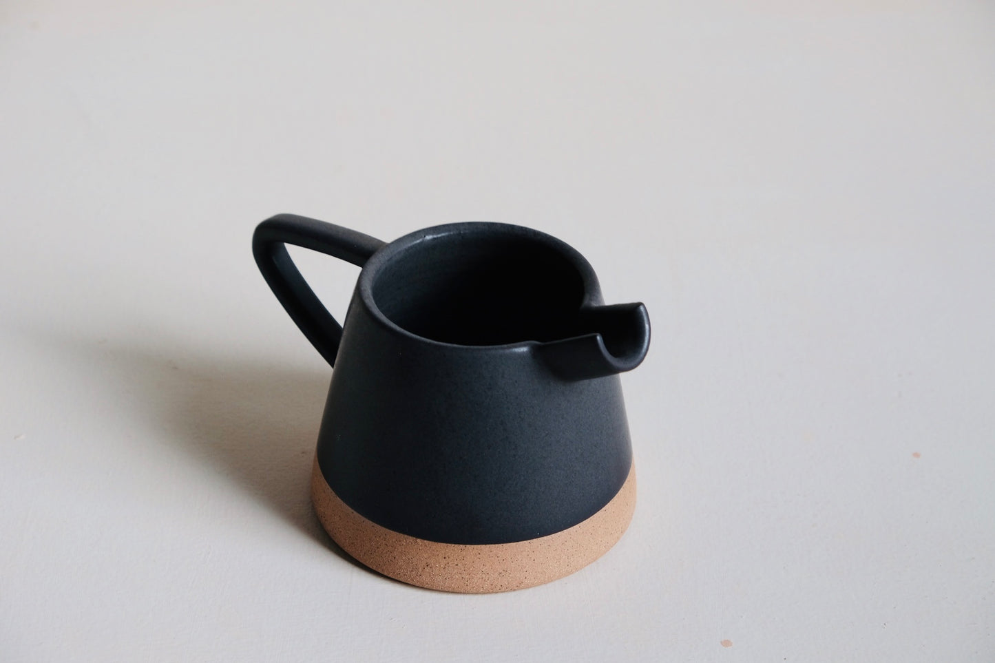 Black ceramic pitcher with cork base on a light gray background