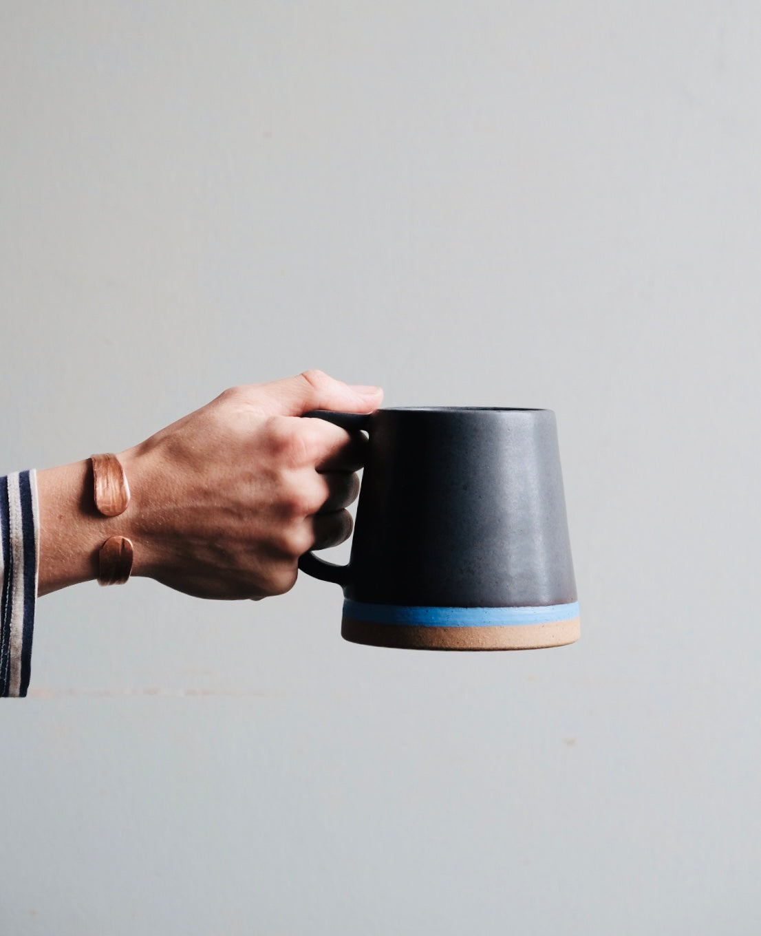 Black mug with blue stripe in a hand