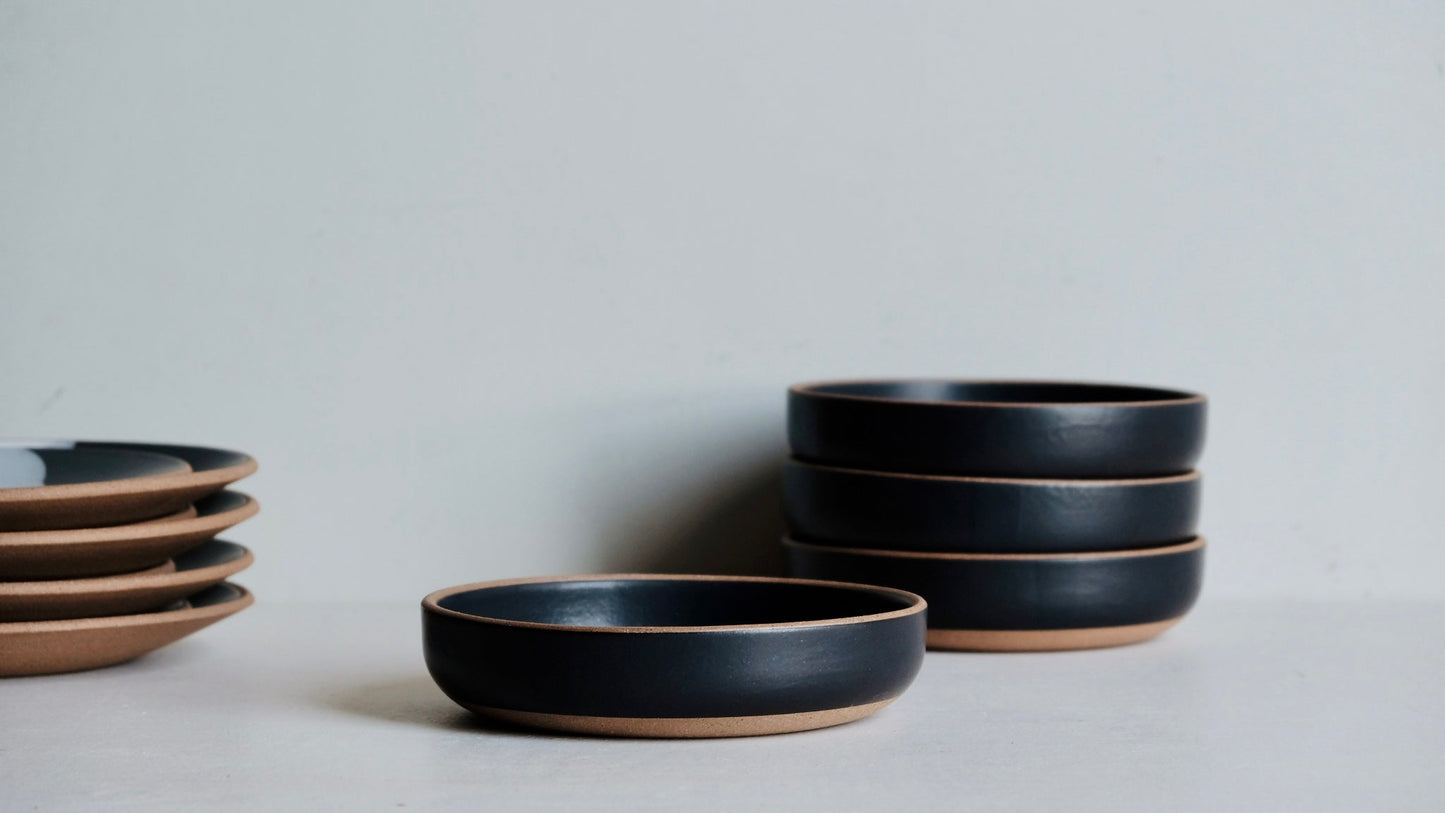 A black ceramic bowl with a beige rim, part of a set, displayed against a neutral background.